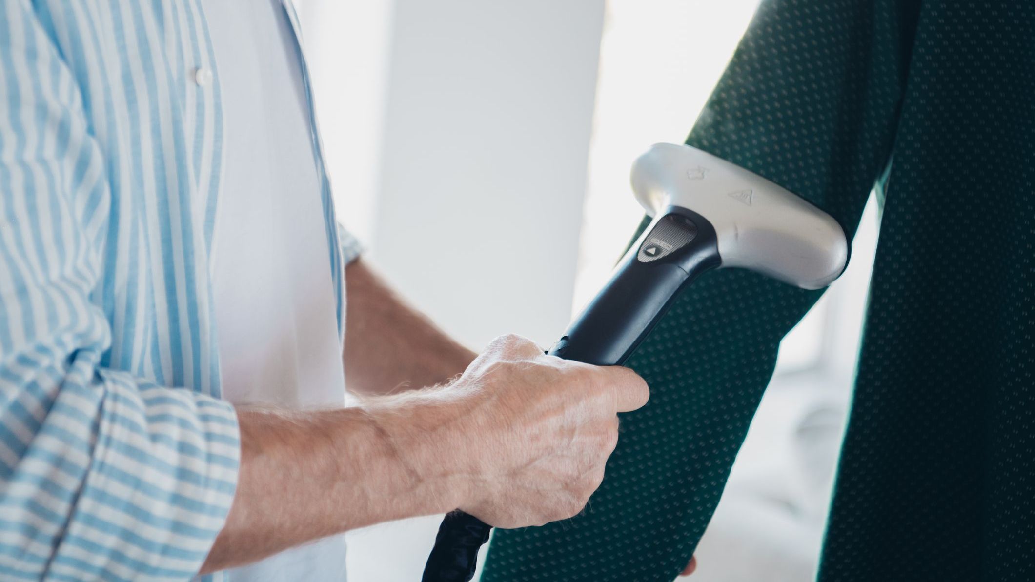 Elderly Man Using a Garment Steamer to Smooth Wrinkles in Clothing in a Cozy Indoor Setting