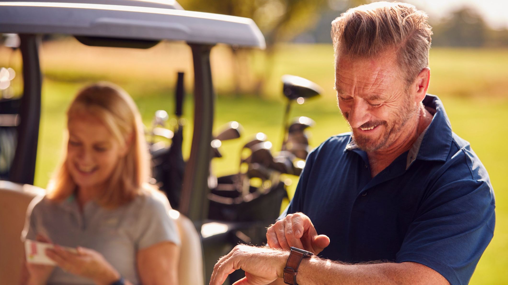 Man Checking Watch As Mature Couple Sit In Buggy And Play Round Of Golf Together
