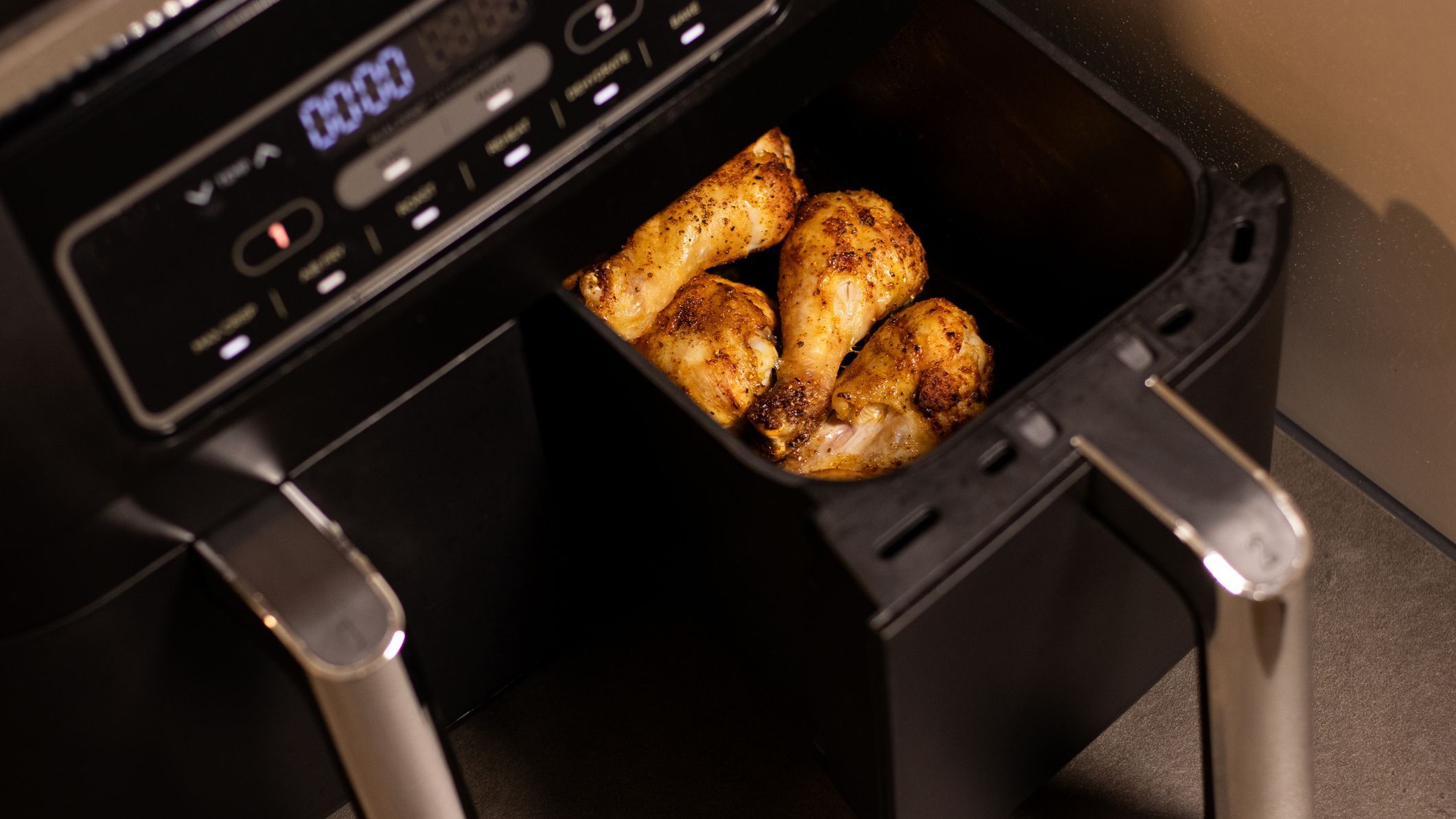 Close up an open black air fryer with roasted chicken drumsticks inside