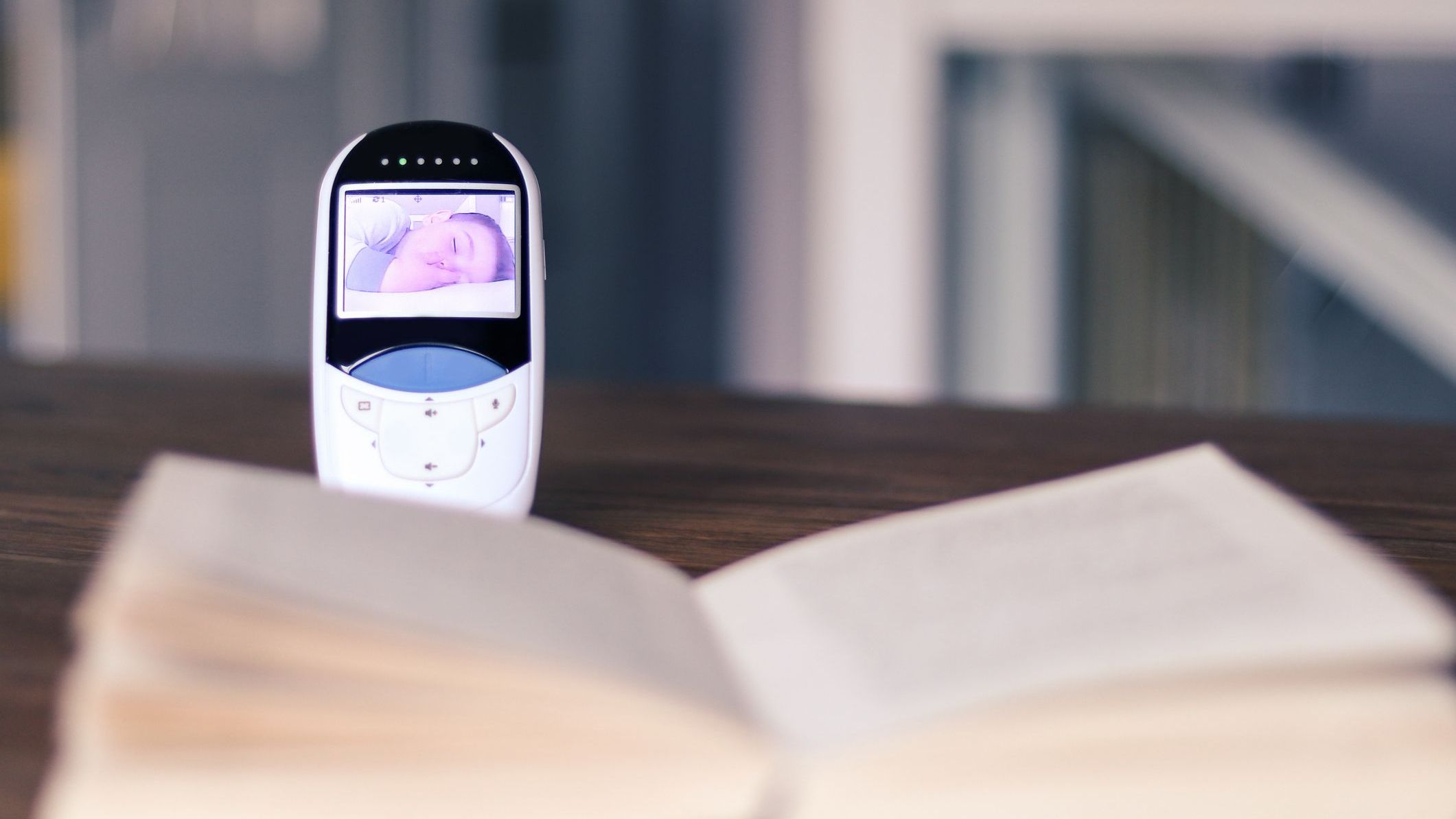 Video baby monitor with image of sleeping baby on the screen on the table with open book. Mother relax time during child daytime sleep. Baby