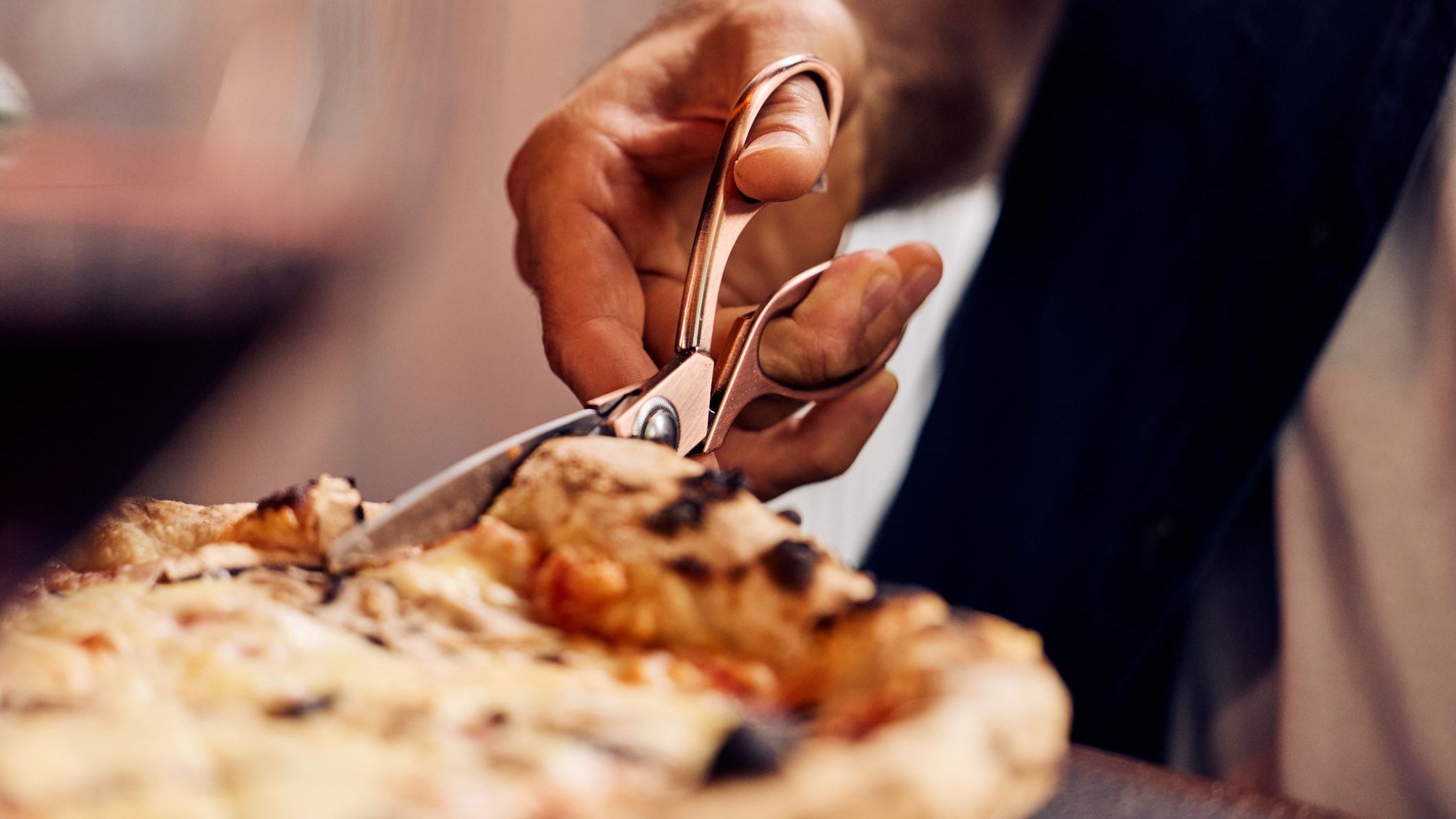Hands Cutting Pizza With Scissors in a Casual Dining Setting