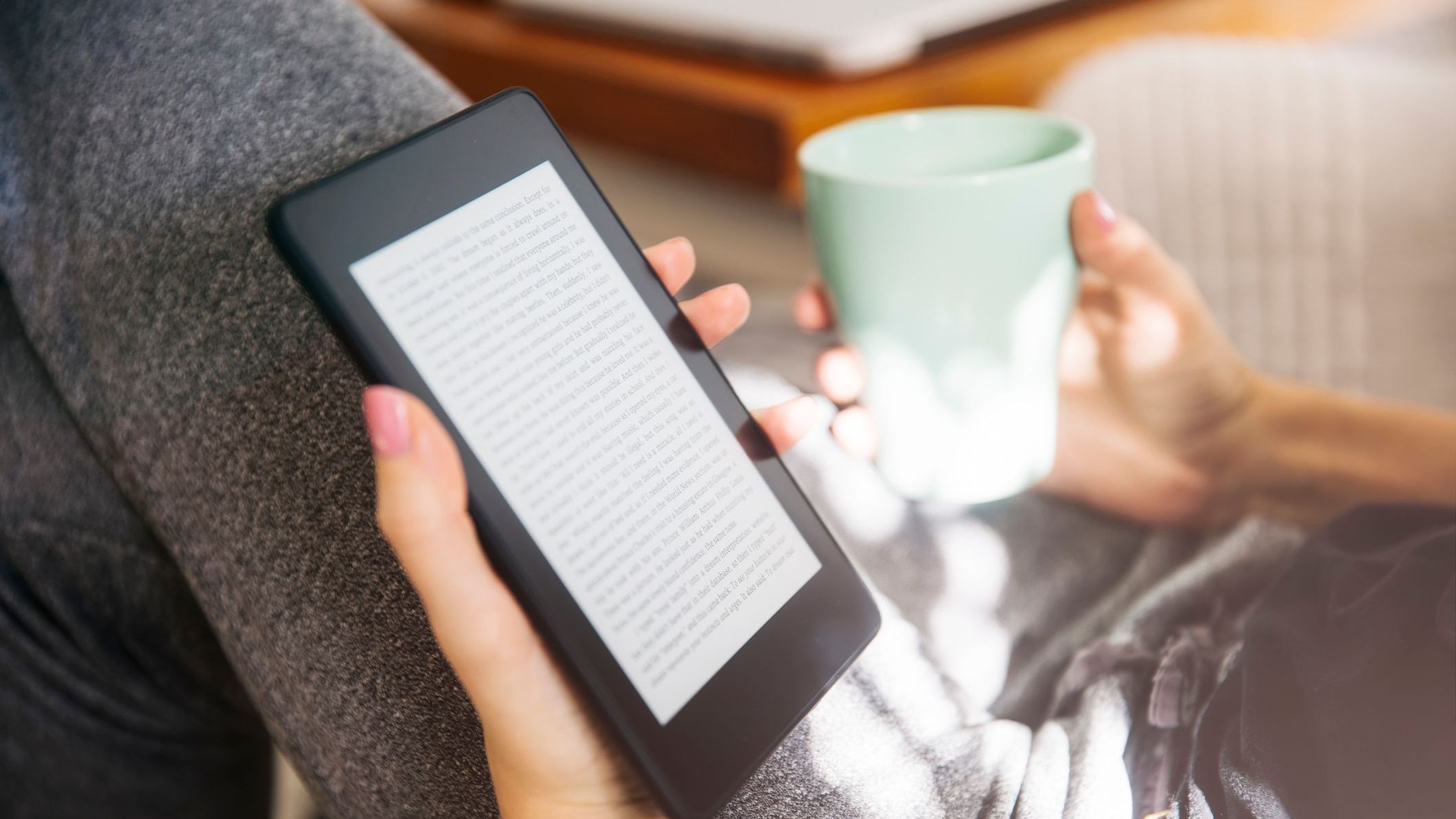 Young woman drinking coffee and using an ebook reader in the sofa