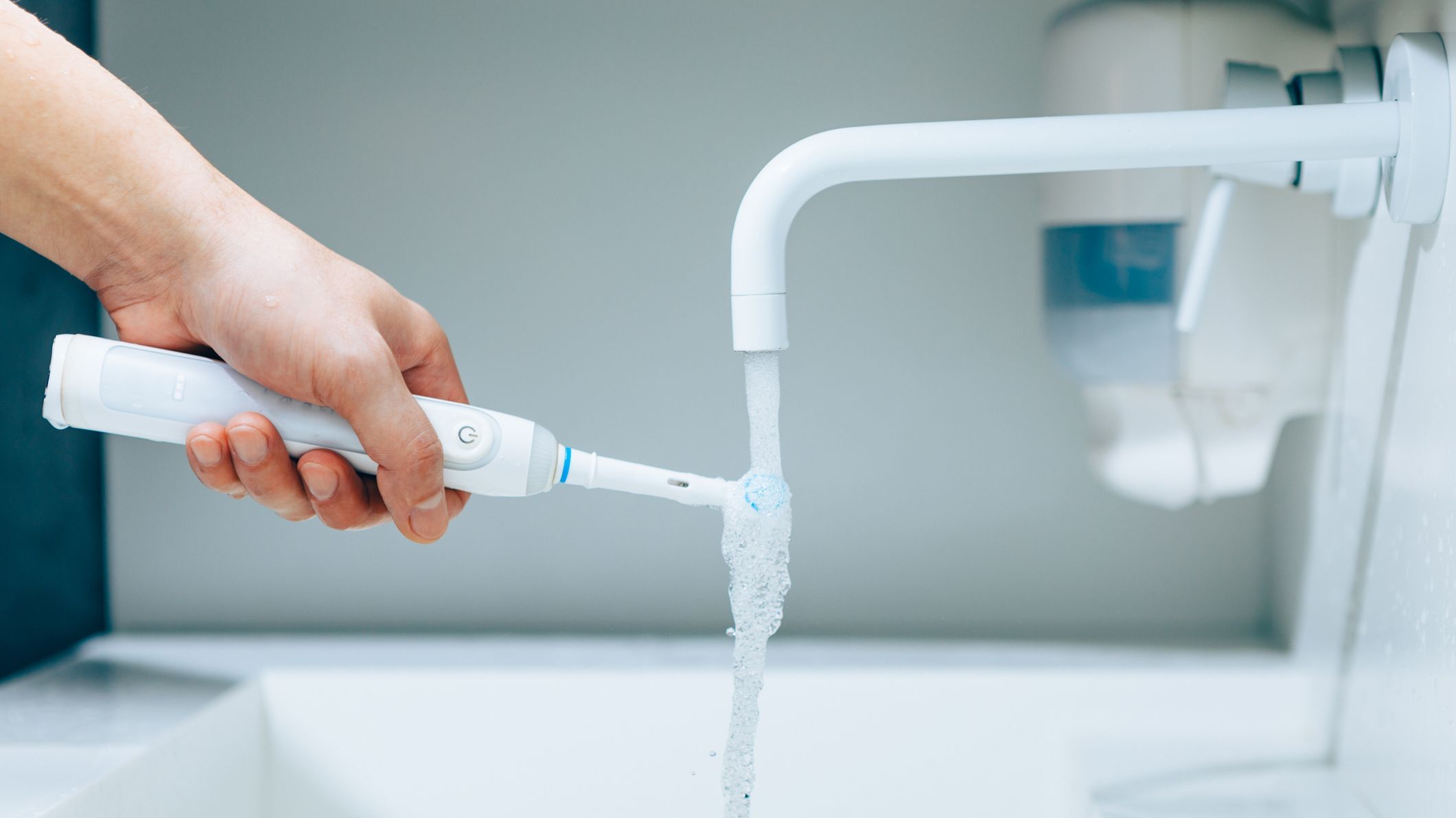hand holding a toothbrush under flowing water from faucet in a bathroom, close-up view