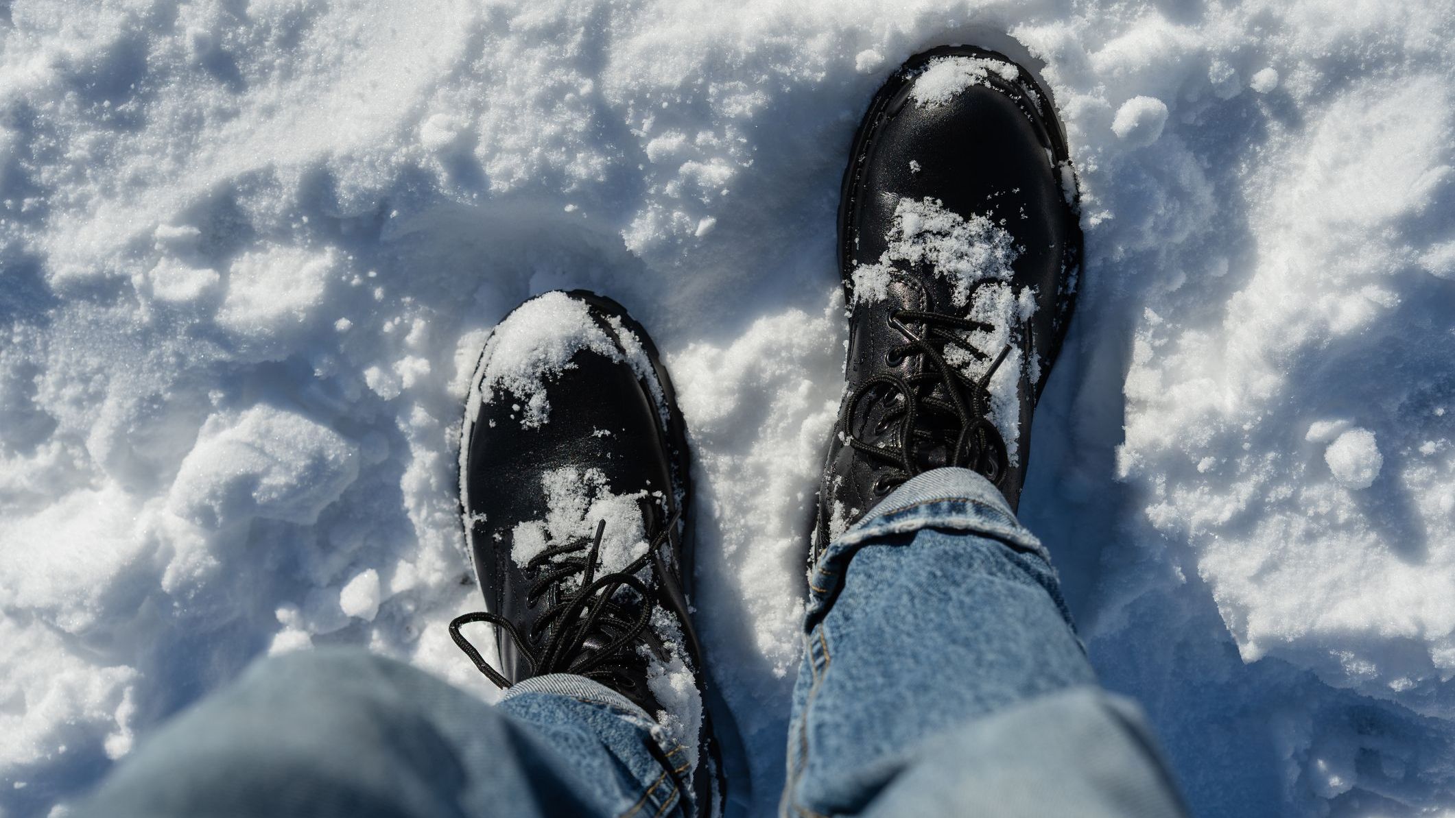Top view of black winter boots in snow on a sunny day.