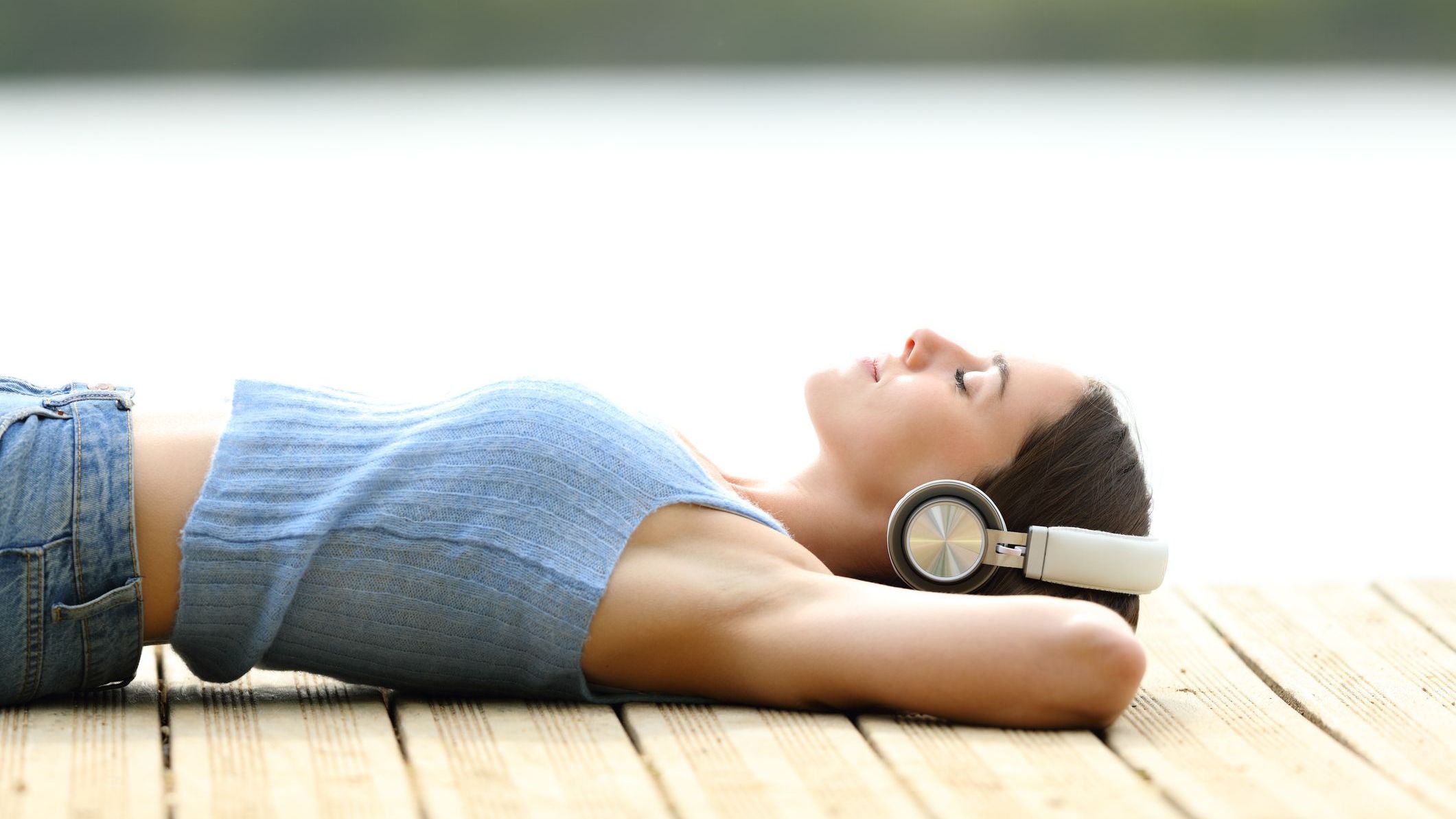 Relaxed woman listening to music lying on a pier