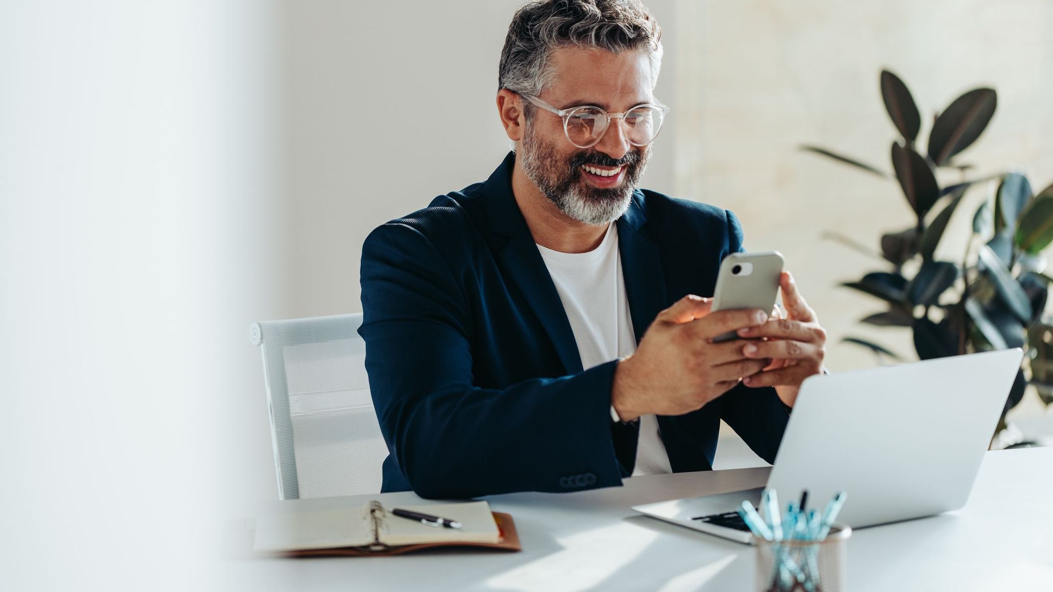 Focused professional man smiling at smartphone in bright modern office