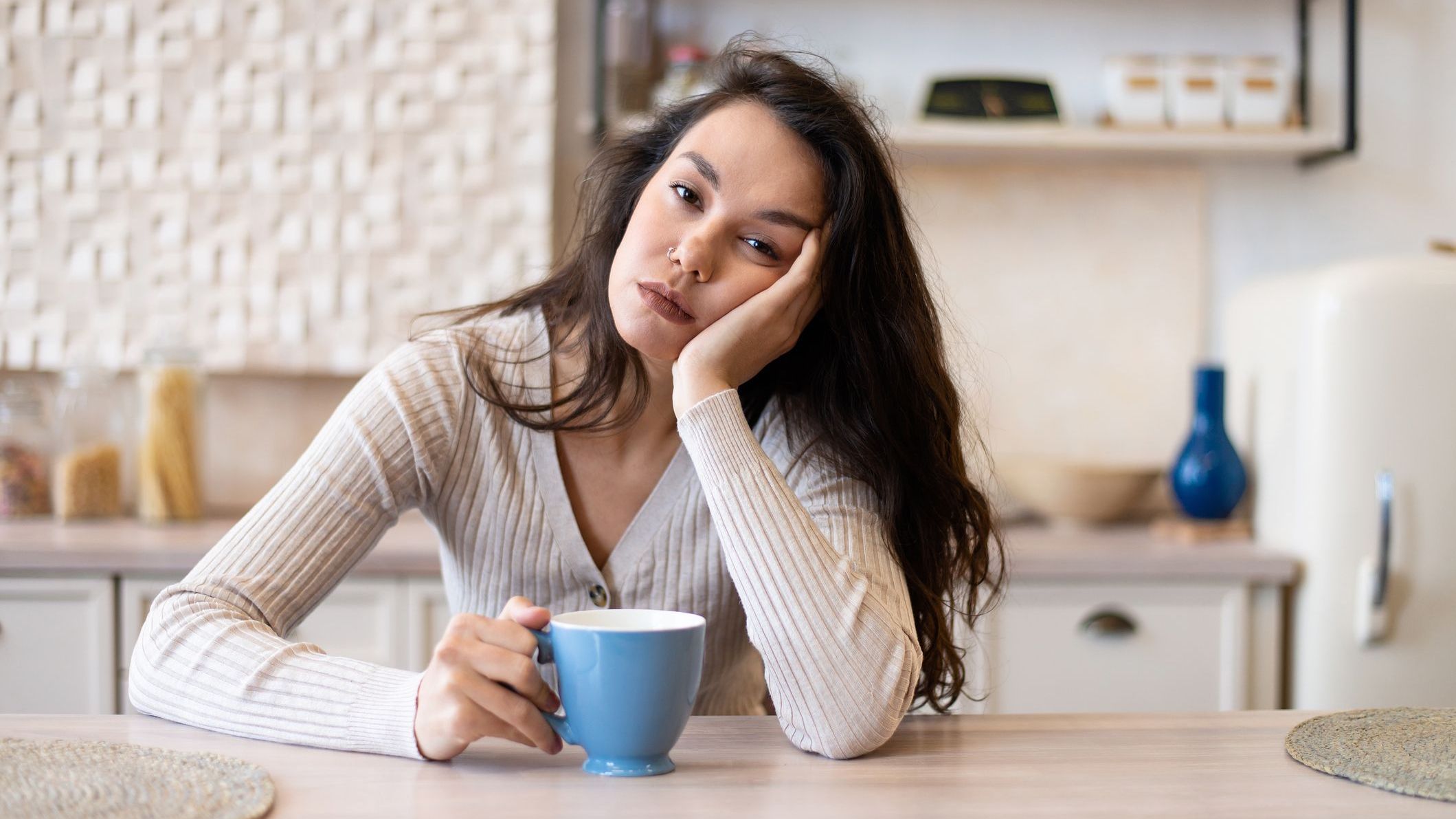 Tired and sleepy woman drinking coffee in the morning, feeling exhausted, suffering from insomnia and sleeping disorder, sitting in kitchen