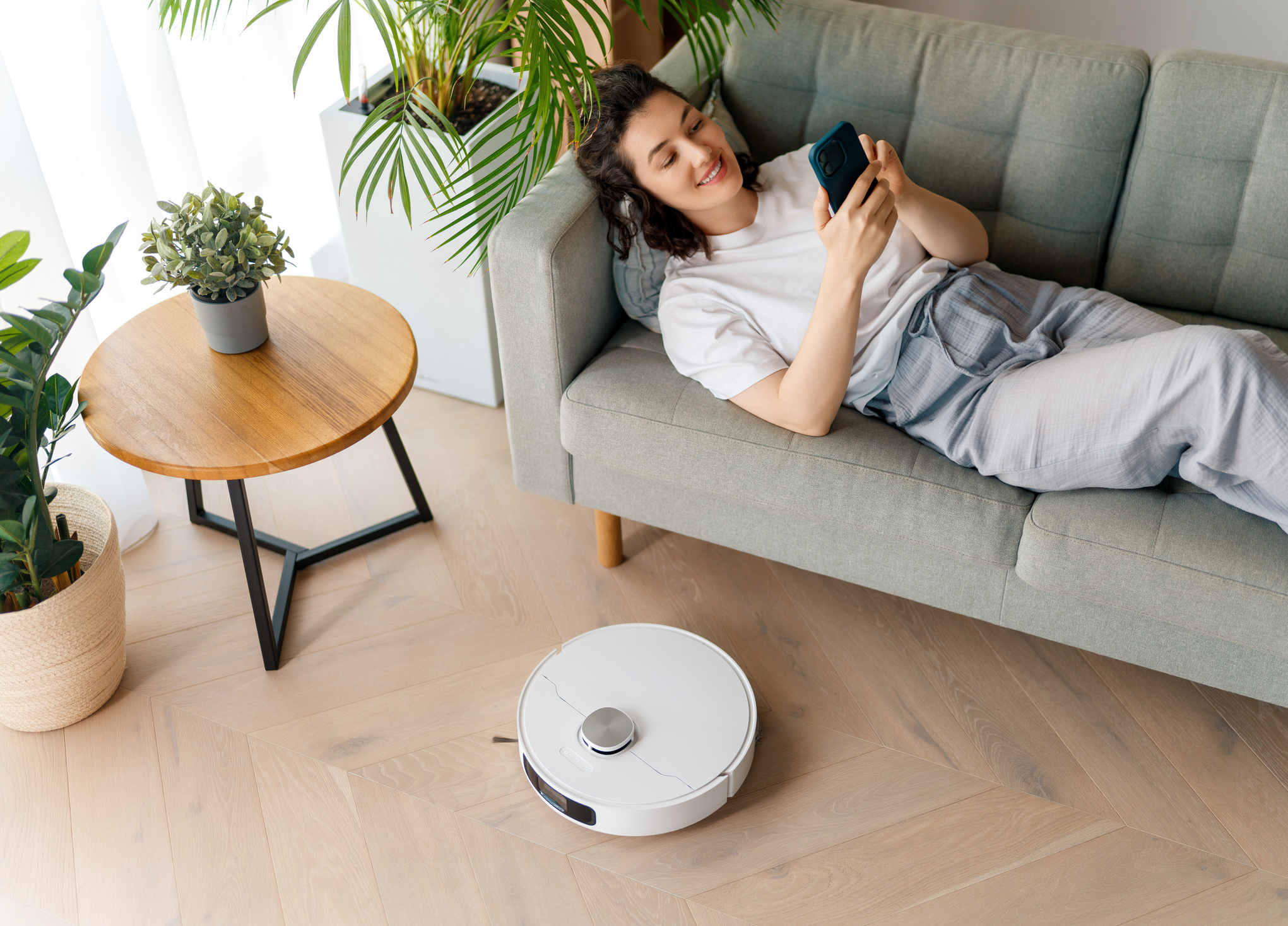 kvinde slapper af på sofaen mens en robotstøvsuger gør rent