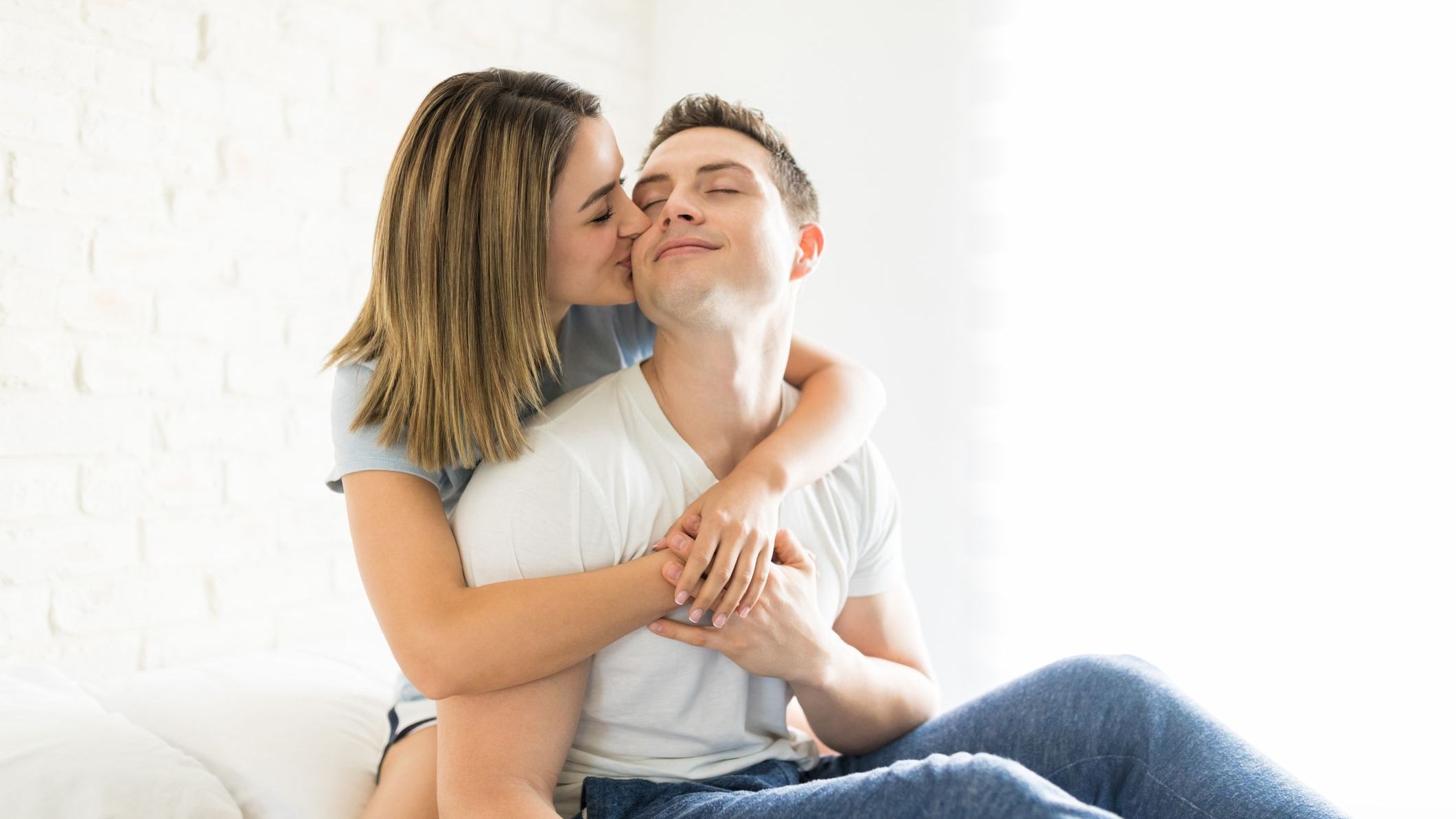 Young woman showing love and affection by kissing man on cheek in bedroom