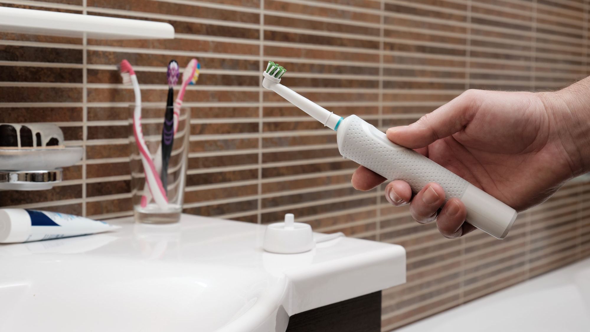 Mans hand holding electric toothbrush against bathroom background