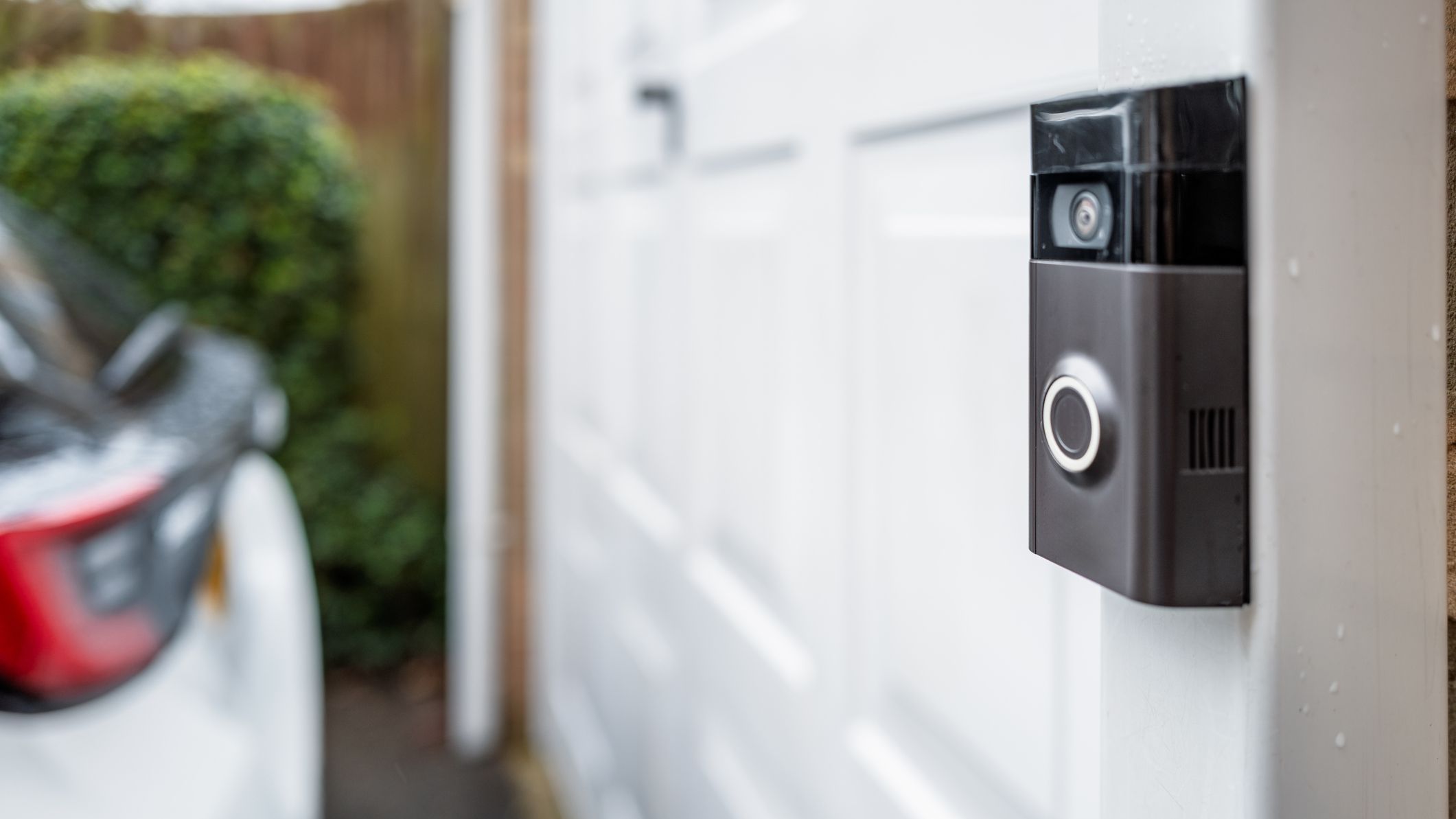 Shallow focus of a popular, battery powered wireless doorbell and integral camera seen located on a driveway, near a side gate entrance