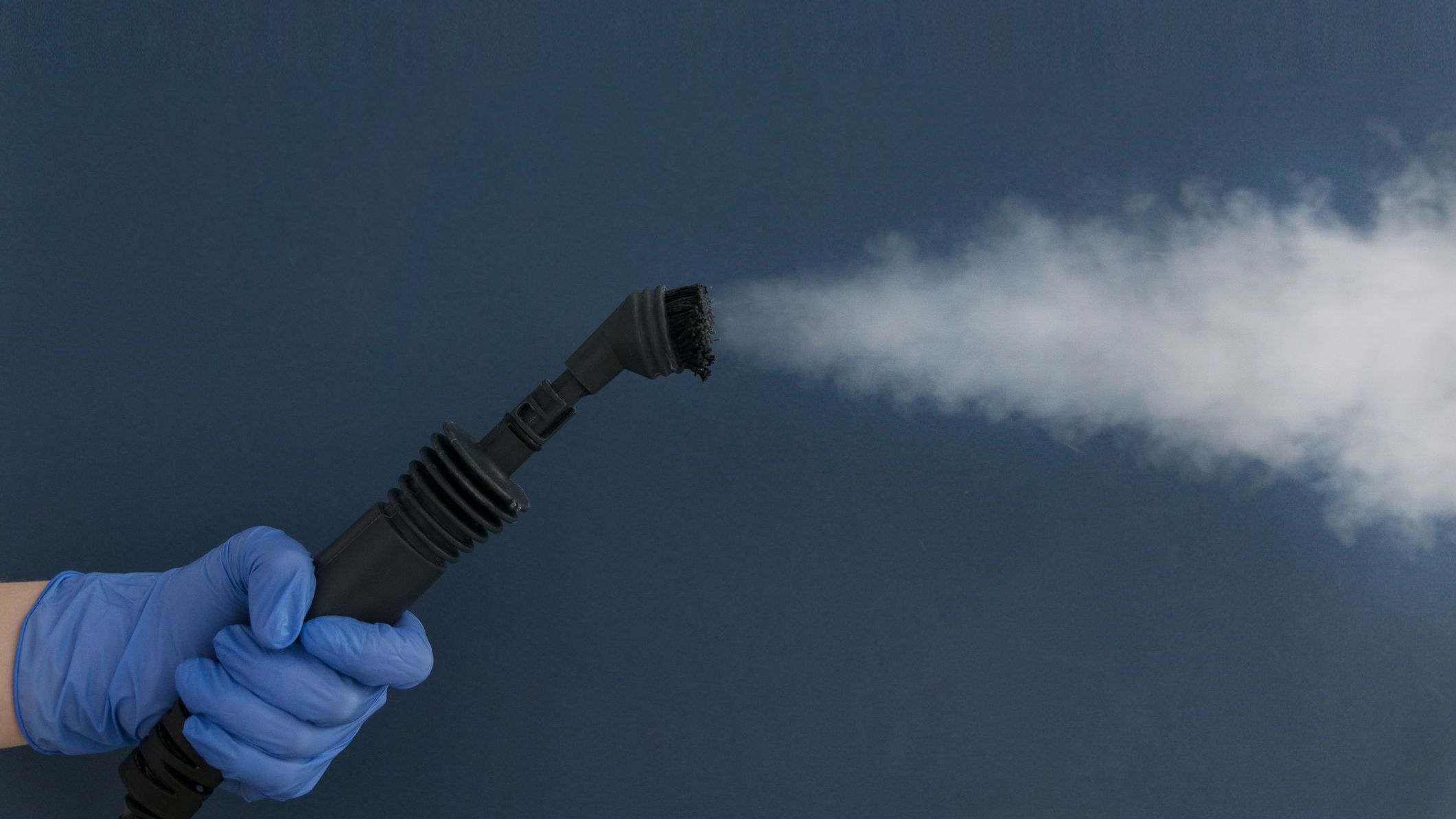 Female hand in blue glove hold hose with brush of home steam generator on blue background