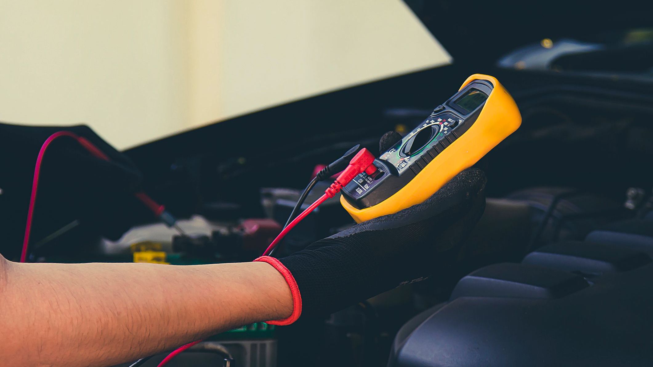 Mechanic hands using digital multimeter to check car battery voltage in auto repair shop