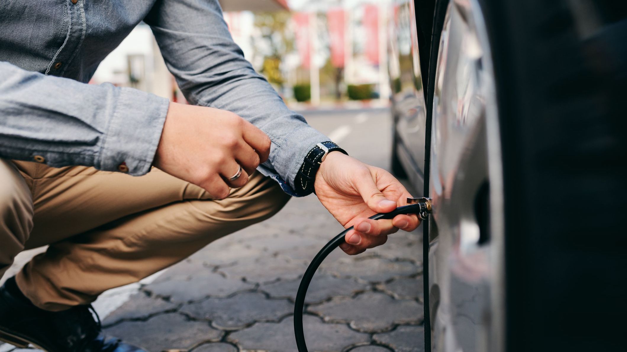Close up of man crouching on the gas station and inflating tire