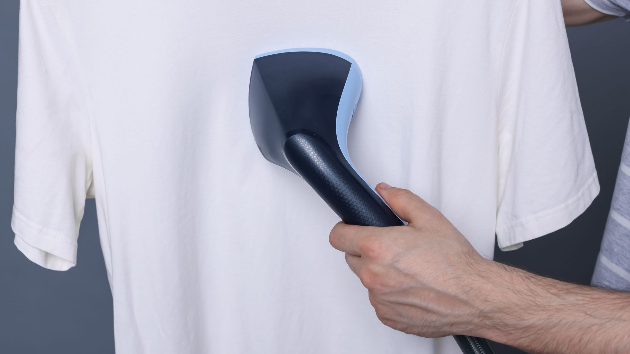 Man steaming t-shirt with stand steamer on grey background, closeup