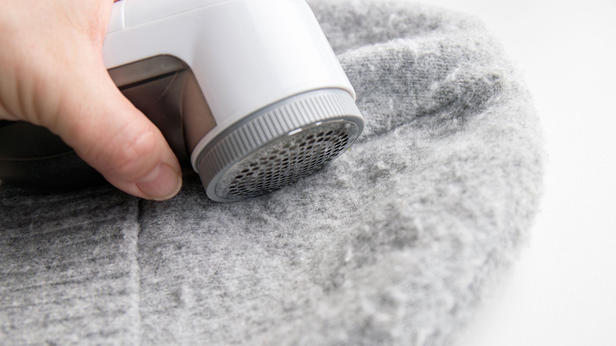 Person hand using sheaving lint balls from winter hat with lint shaver machine tool.